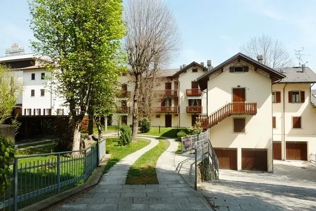 Villaggio residenziale con case bianche, giardini curati e vialetti in pietra circondati da alberi