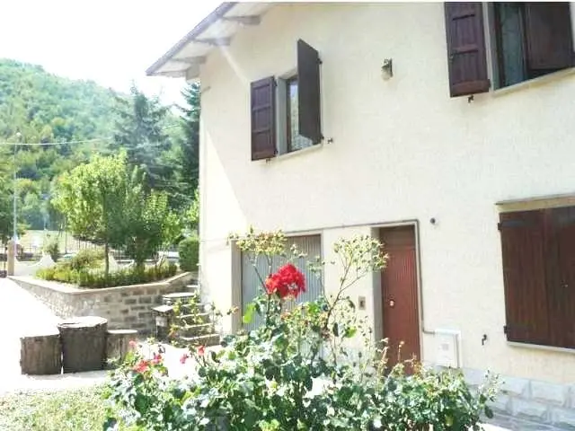 Villa a due piani con persiane scure e giardino fiorito con rose rosse davanti all'ingresso