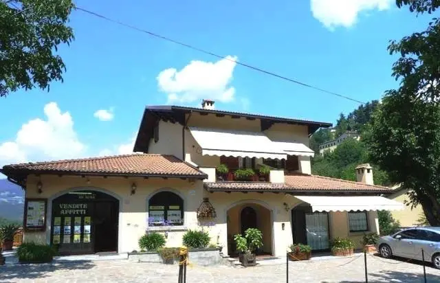 Villa moderna a due piani con tetto spiovente e giardino curato, circondata da alberi sotto un cielo azzurro con nuvole