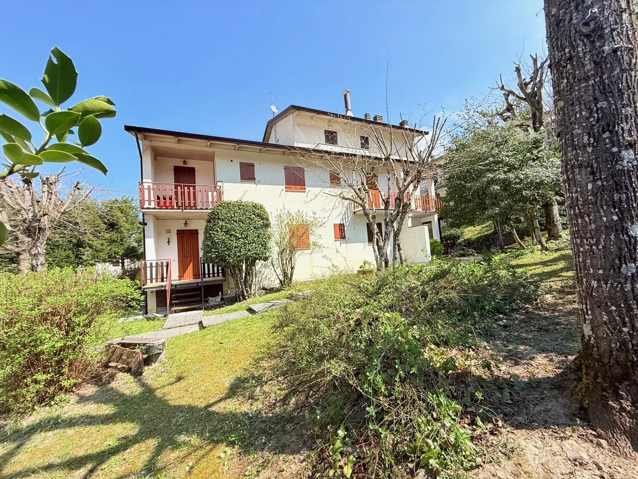 Casa tradizionale con giardino verde, alberi da frutto in fiore e prato curato sotto cielo azzurro