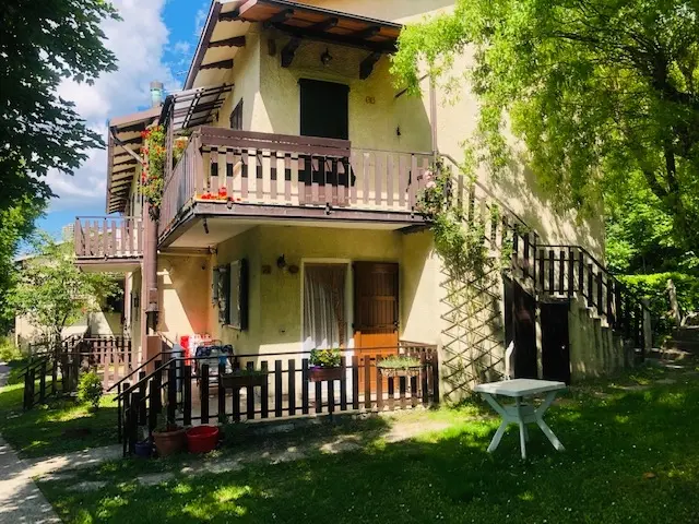 Villa a due piani con balconi in legno e giardino verde sotto un cielo azzurro