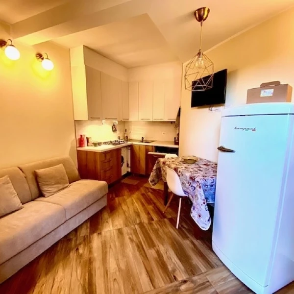 Monolocale con divano beige, angolo cottura in legno e frigorifero bianco con pavimento effetto parquet