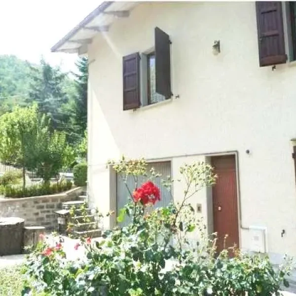 Villa a due piani con persiane scure e giardino fiorito con rose rosse davanti all'ingresso