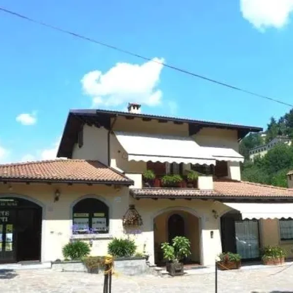 Villa moderna a due piani con tetto spiovente e giardino curato, circondata da alberi sotto un cielo azzurro con nuvole