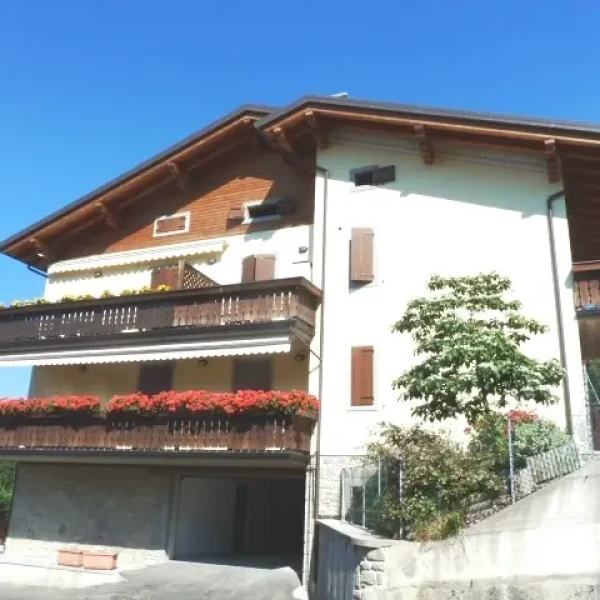 Casa alpina bianca con balconi in legno decorati da fiori rossi, tetto spiovente e cielo azzurro