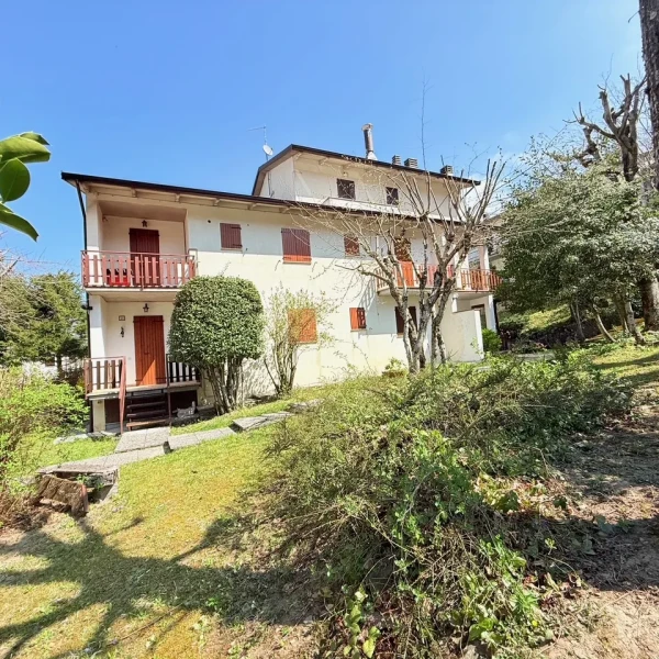 Casa tradizionale con giardino verde, alberi da frutto in fiore e prato curato sotto cielo azzurro