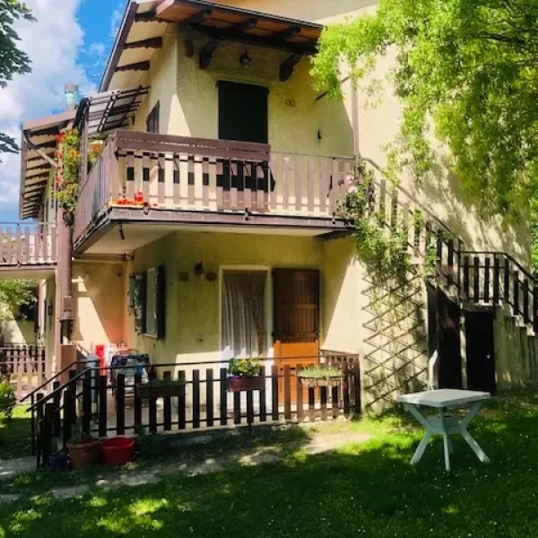 Villa a due piani con balconi in legno e giardino verde sotto un cielo azzurro